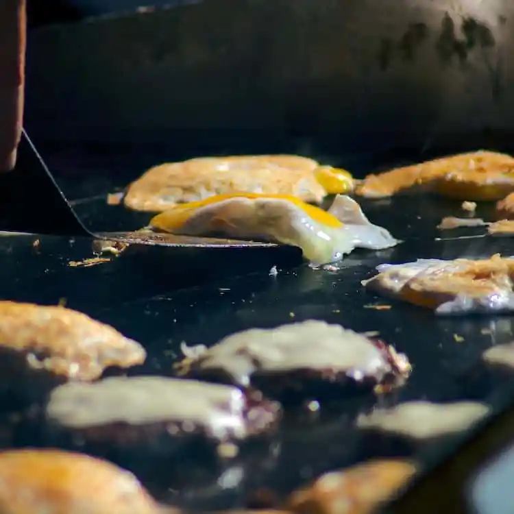 Frying eggs and burger patties with cheese on a griddle